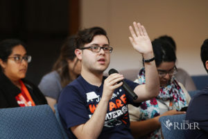 A picture of a young man raising his hand during a forum